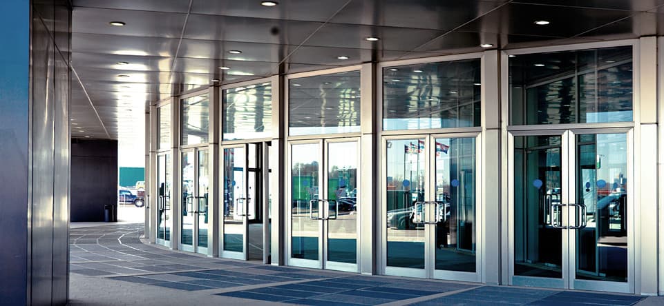 Curved row of commercial glass entry doors with metal frames and transoms
