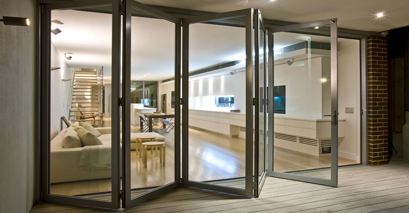 Multi-panel folding glass door opening from a lit interior onto a wooden deck
